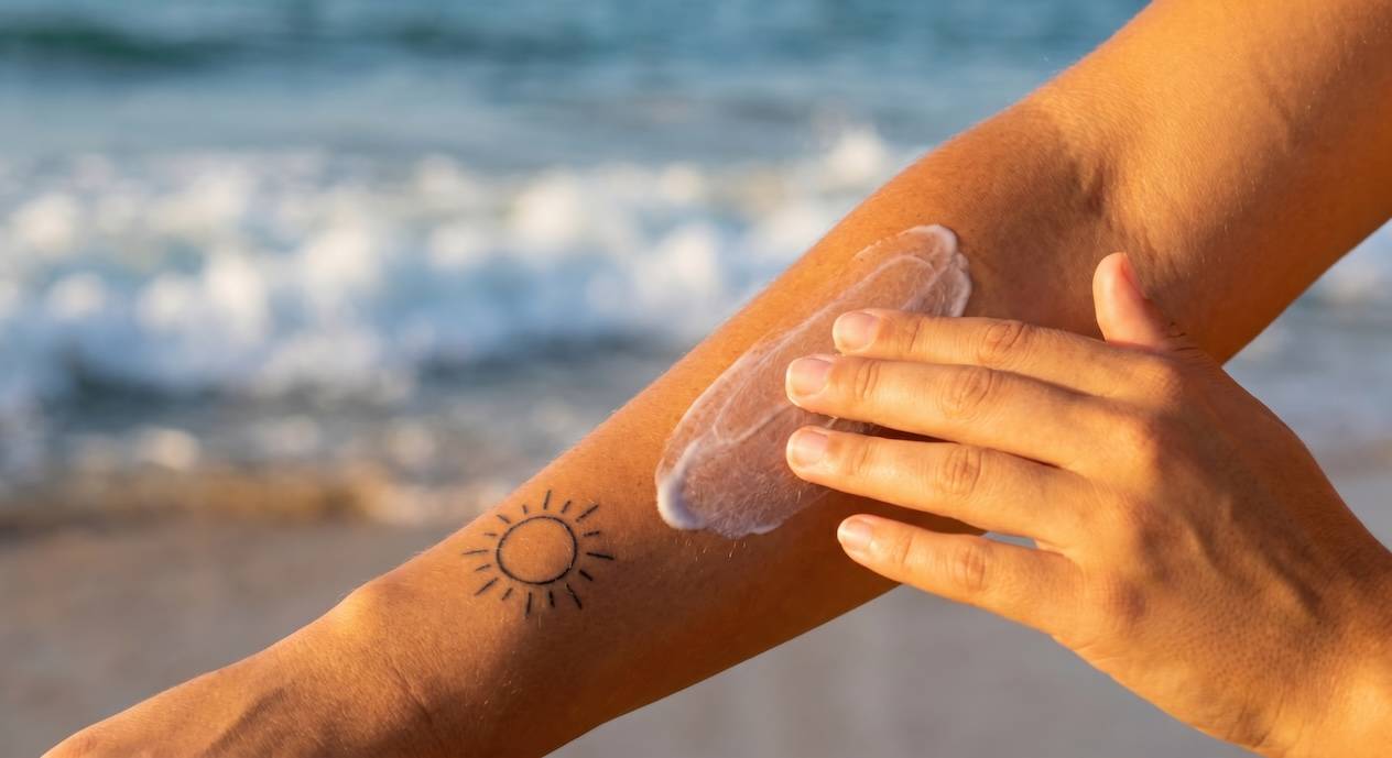 Arm mit Sonnencreme und Sonne-Tattoo am Strand