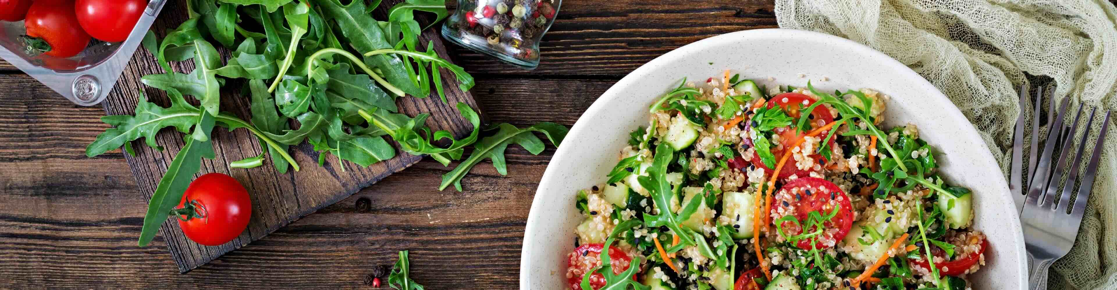 Ein gesunder Quinoa-Salat mit Tomaten, Gurken und Rucola in einer Schüssel.