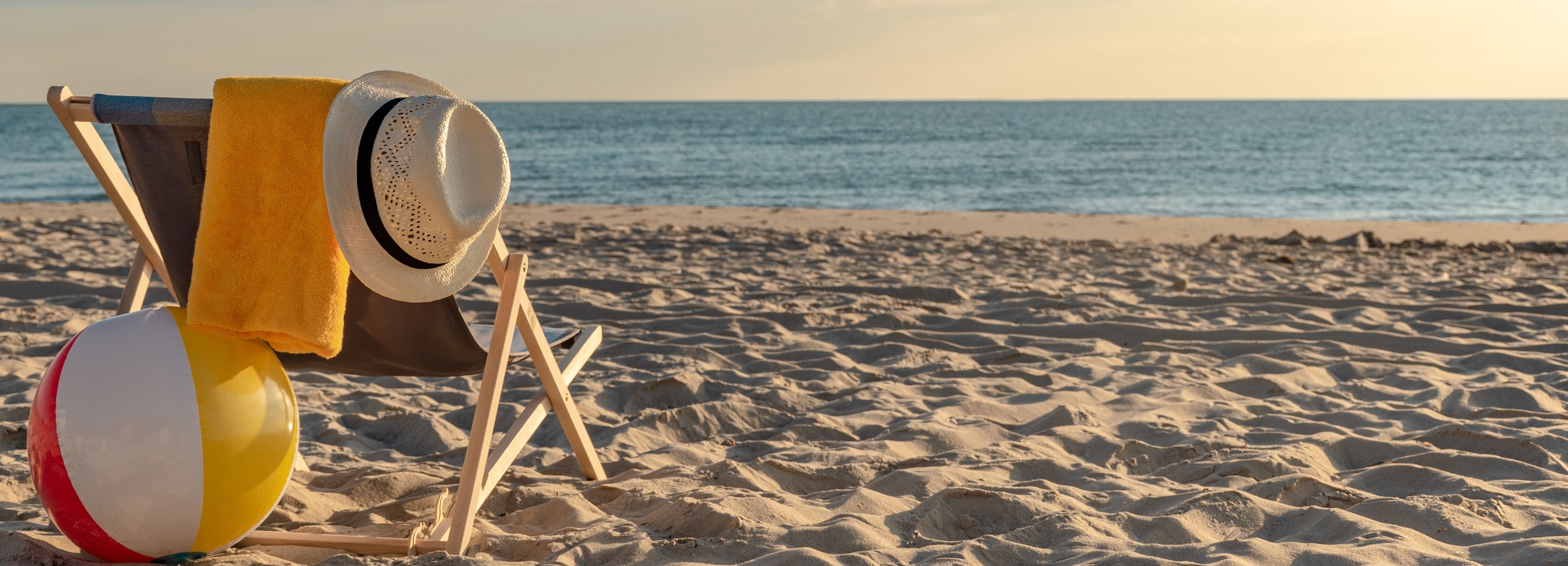 Liegestuhl mit Handtuch, Hut und Wasserball am Strand mit Meerblick.