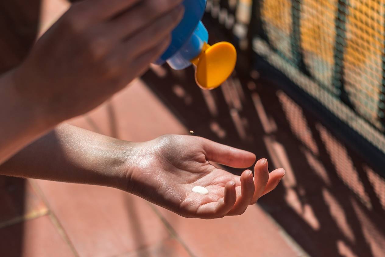 Eine Hand drückt Sonnencreme aus einer Flasche in die andere Hand.
