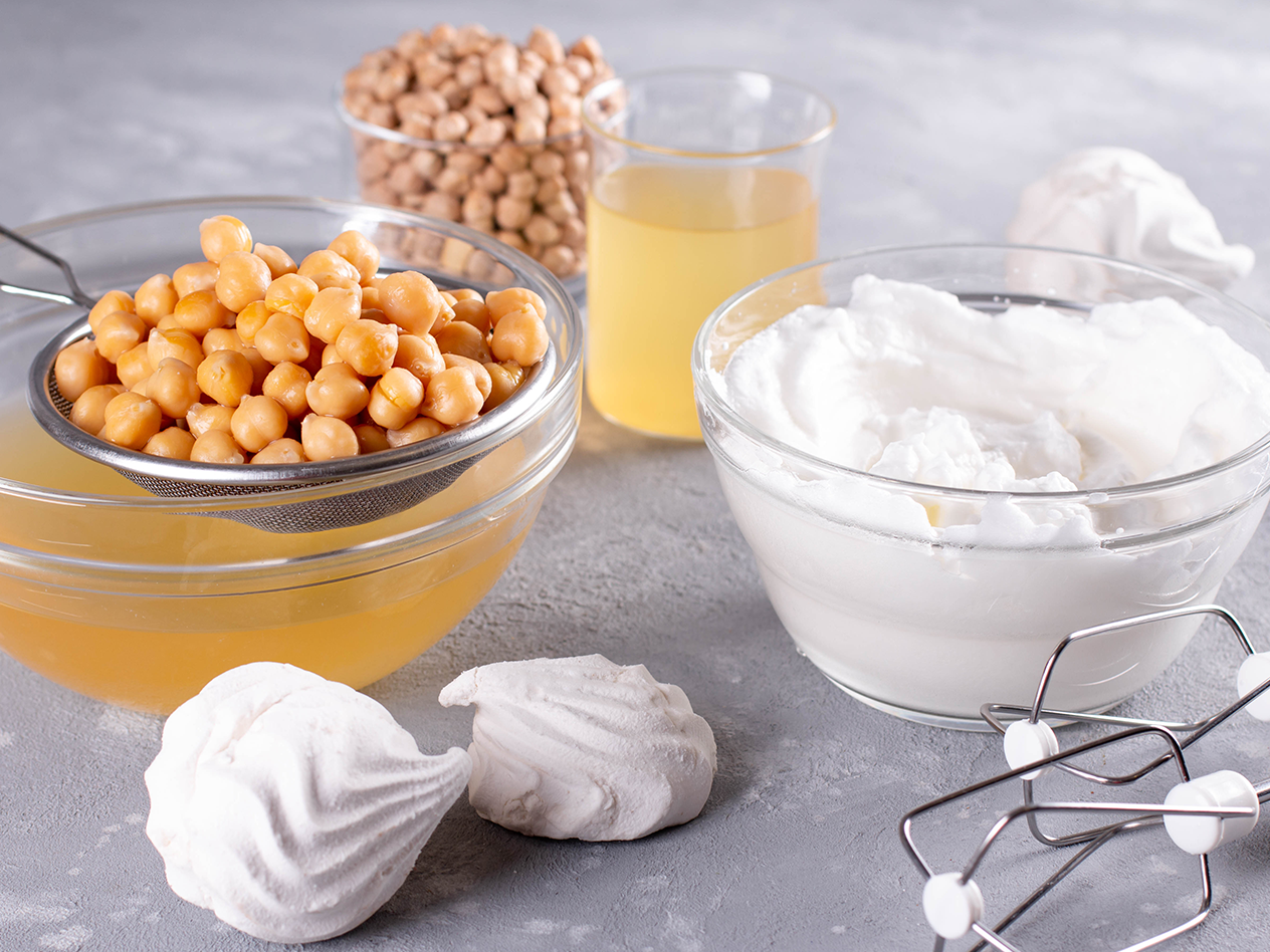 Kichererbsen, Aquafaba und geschlagenes Aquafaba in Schüsseln mit Baisers und Mixer.