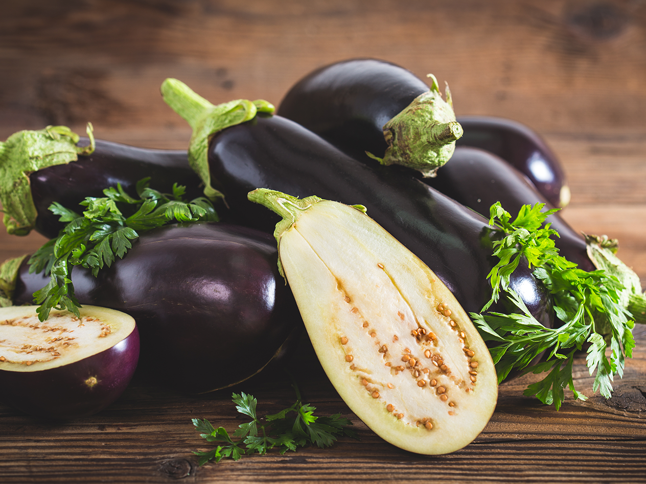 Frische Auberginen, einige halbiert, mit Petersilie auf einem Holztisch.