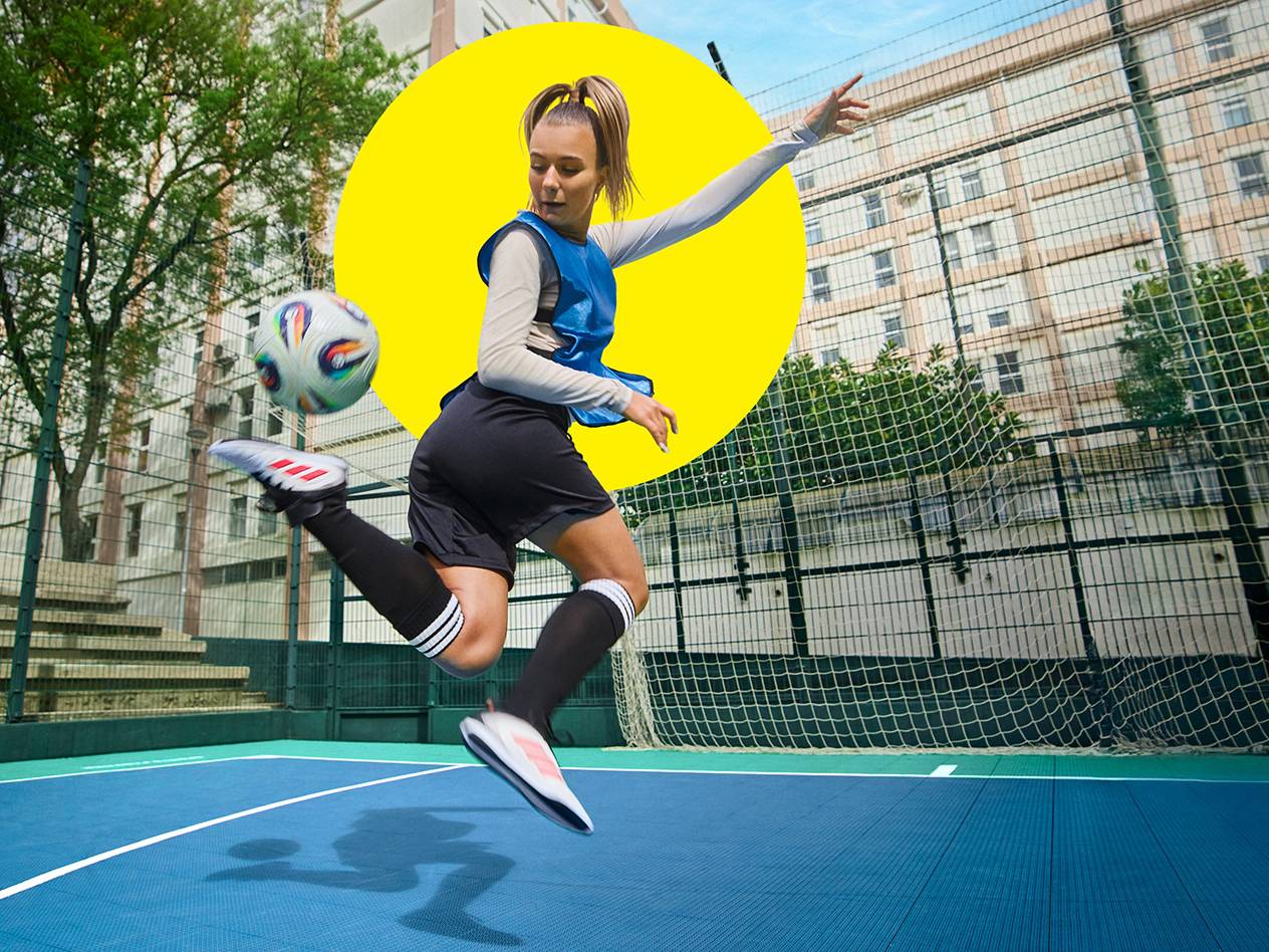 Eine Frau jongliert mit einem Fußball in der Luft auf einem Fußballplatz.