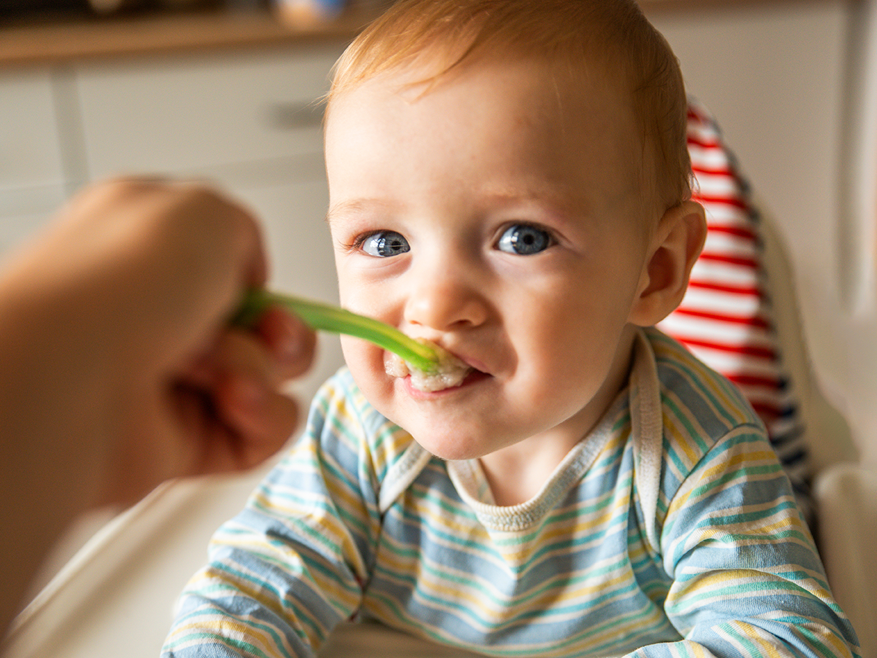 Baby wird mit einem grünen Löffel gefüttert