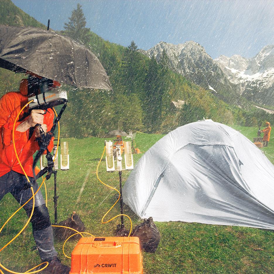 Person in Regenkleidung testet Campingausrüstung im Regen mit Bergen im Hintergrund.
