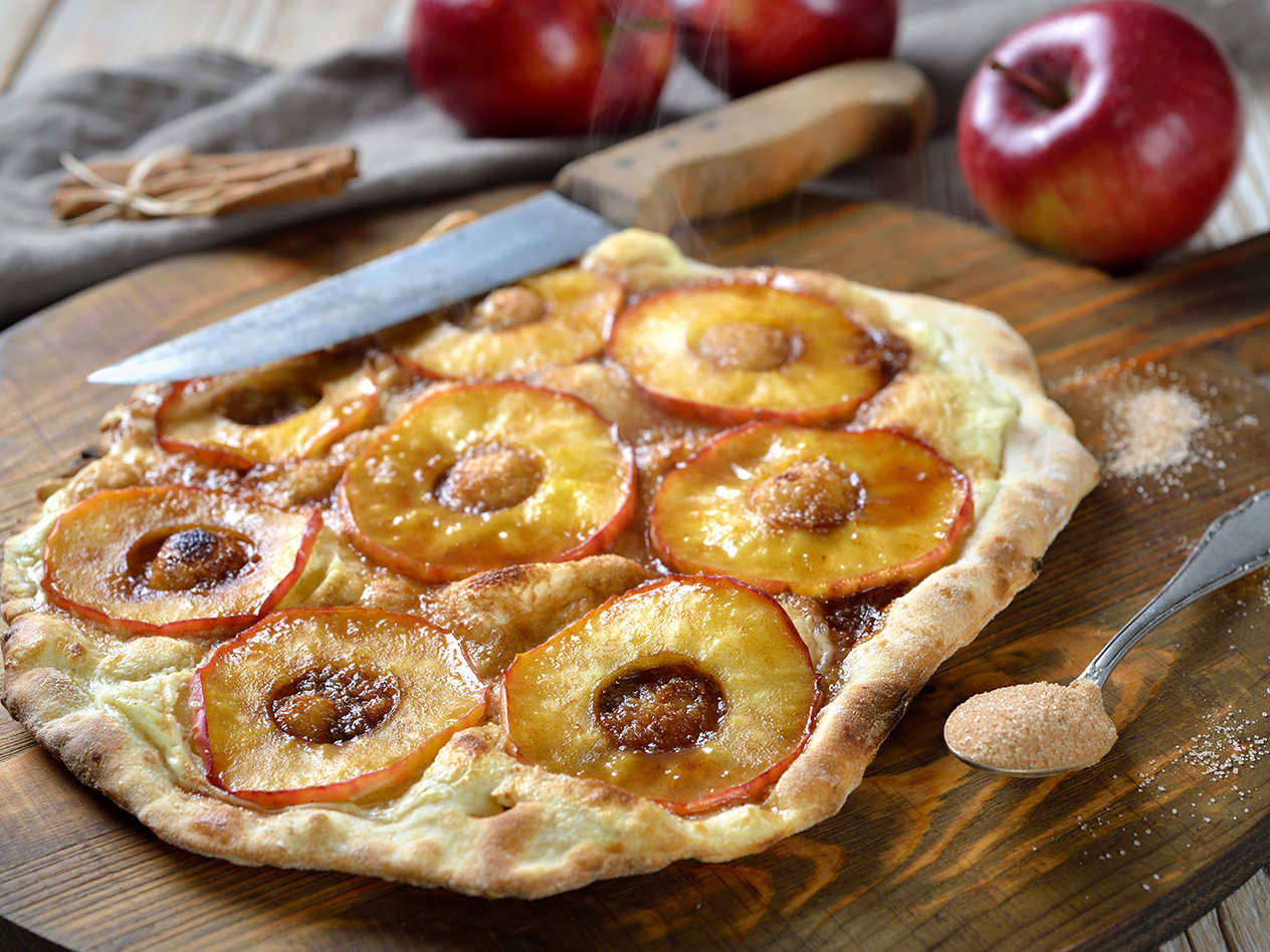 Apfel-Zimtpizza auf Holzbrett mit Äpfeln und Zimtstangen