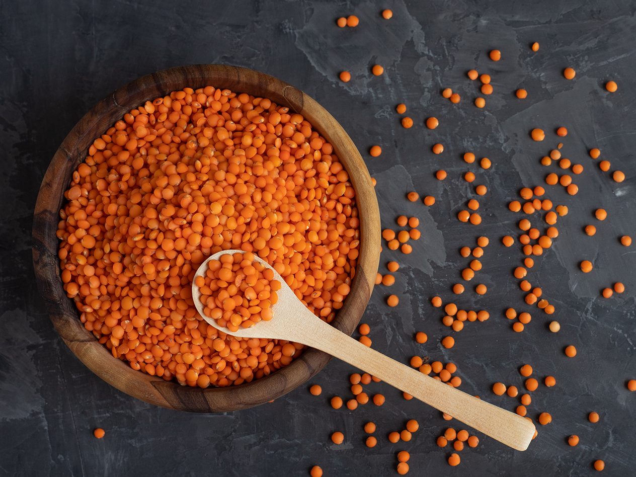 Rote Linsen in einer Holzschale mit einem Holzlöffel auf dunklem Hintergrund.