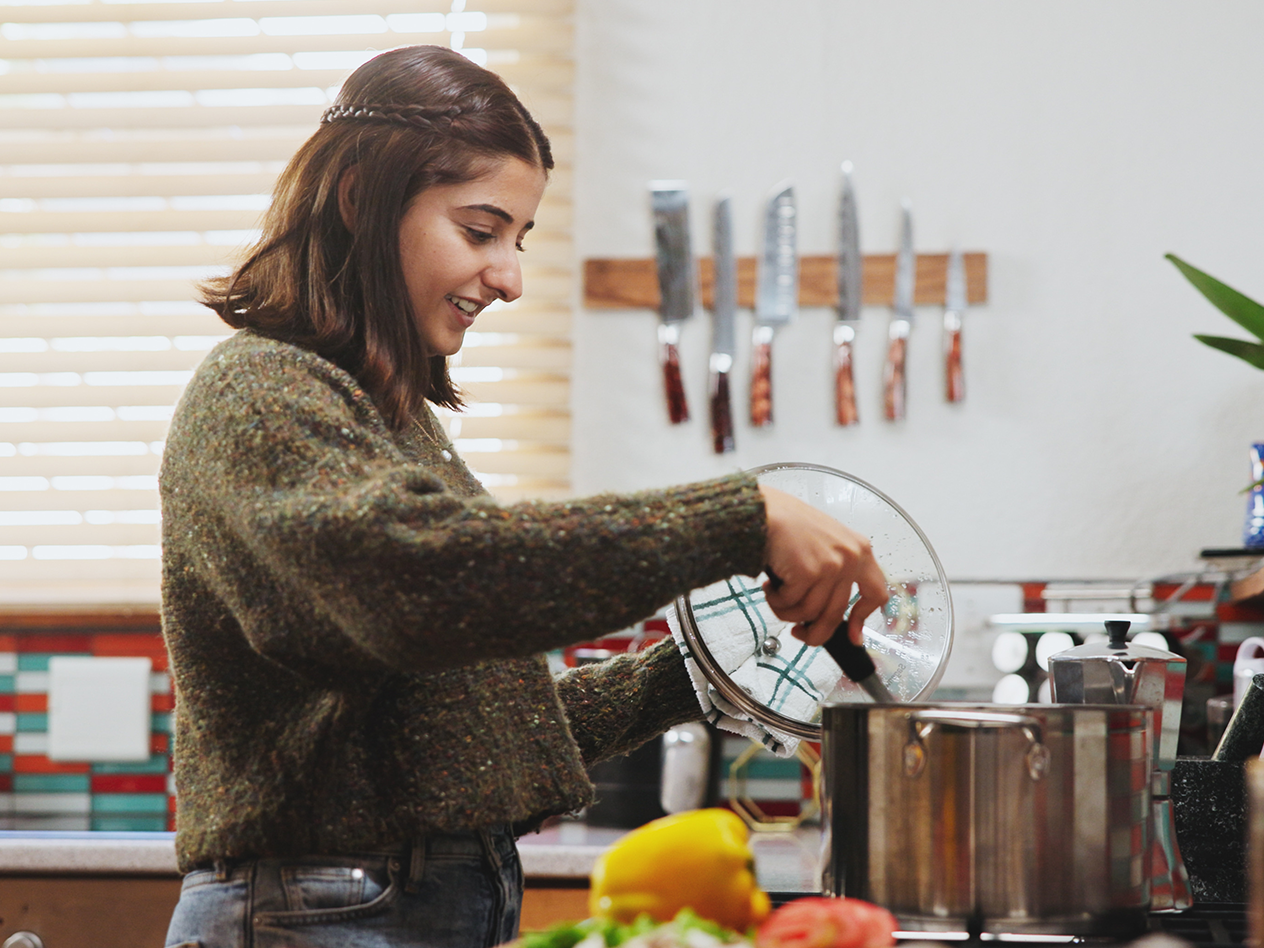 Junge Frau kocht in der Küche, hebt den Deckel von einem Topf.