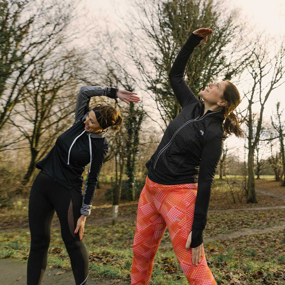 Zwei Frauen in Sportkleidung dehnen sich im Freien.