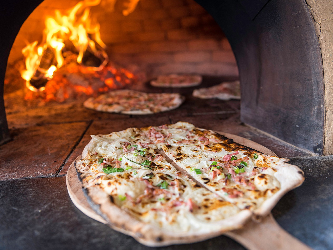 Flammkuchen wird in einem Holzofen mit loderndem Feuer gebacken
