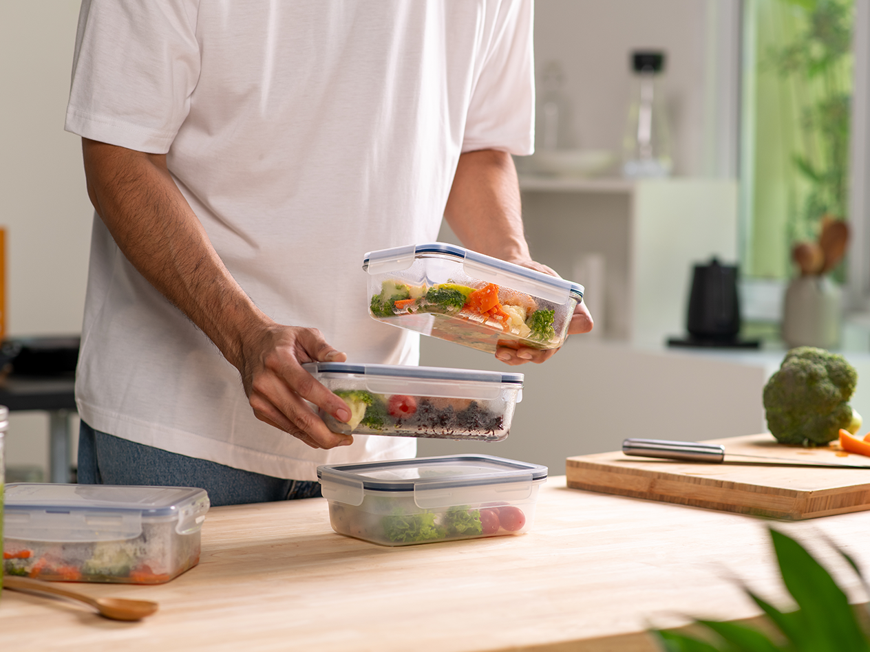 Person bereitet Mahlzeiten in Frischhaltedosen mit Gemüse in einer Küche vor.