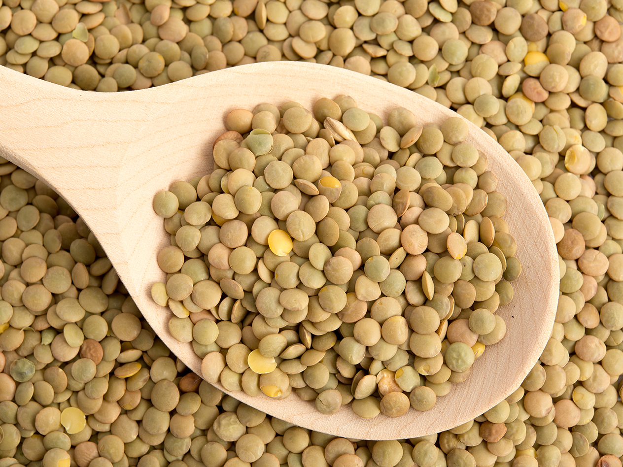 Grüne Linsen auf einem Holzlöffel und verstreut auf einer Oberfläche.