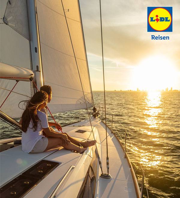 Ein Paar genießt einen Sonnenuntergang auf einem Segelboot während eines Lidl Reisen Urlaubs.