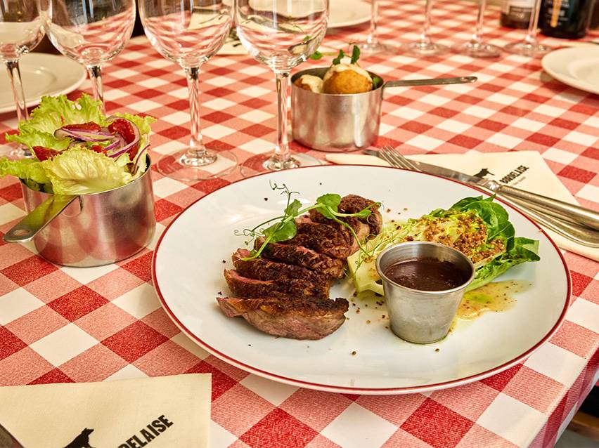Geschnittenes Steak mit Salat, Soße und Beilagen auf einer rot-weiß karierten Tischdecke.