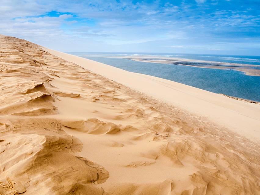 Goldene Sanddüne mit einer blauen Lagune und bewölktem Himmel im Hintergrund.