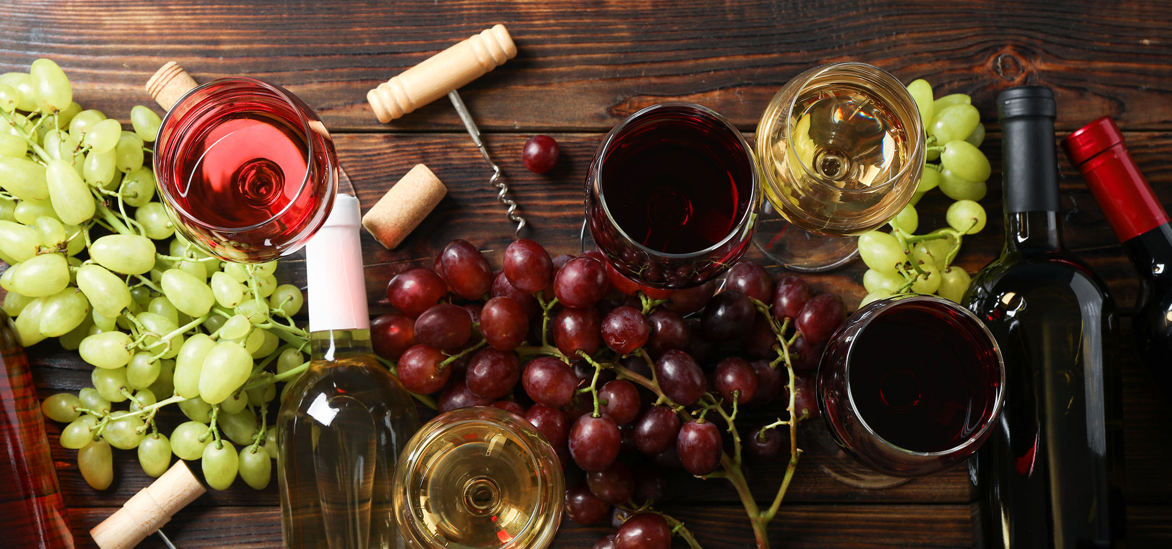 Verschiedene Weine, Trauben und Weinzubehör auf einem Holztisch.