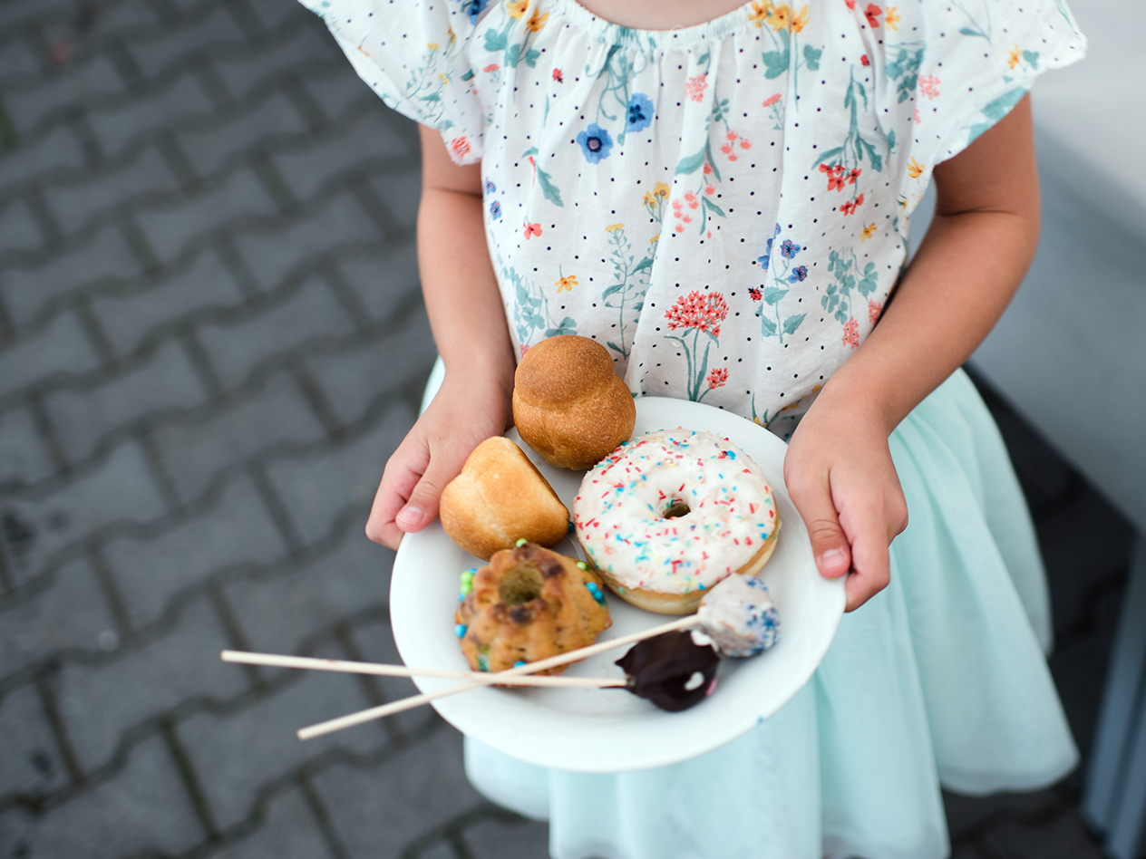 Kind hält einen Teller mit Donuts, Kuchen und Gebäck in den Händen.