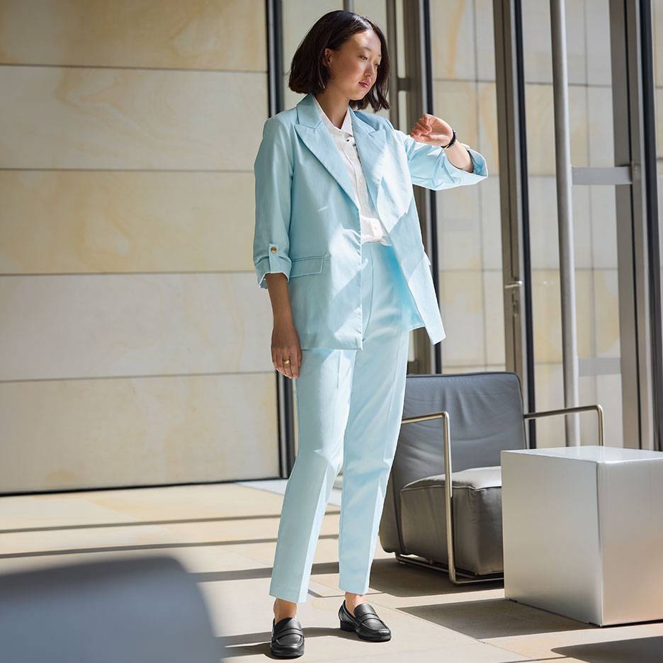 Frau in hellblauem Anzug mit Blazer und Hose, trägt schwarze Loafer.