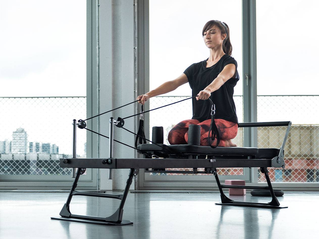Frau macht Pilates-Übungen auf einem Reformer-Gerät mit Stadtkulisse.