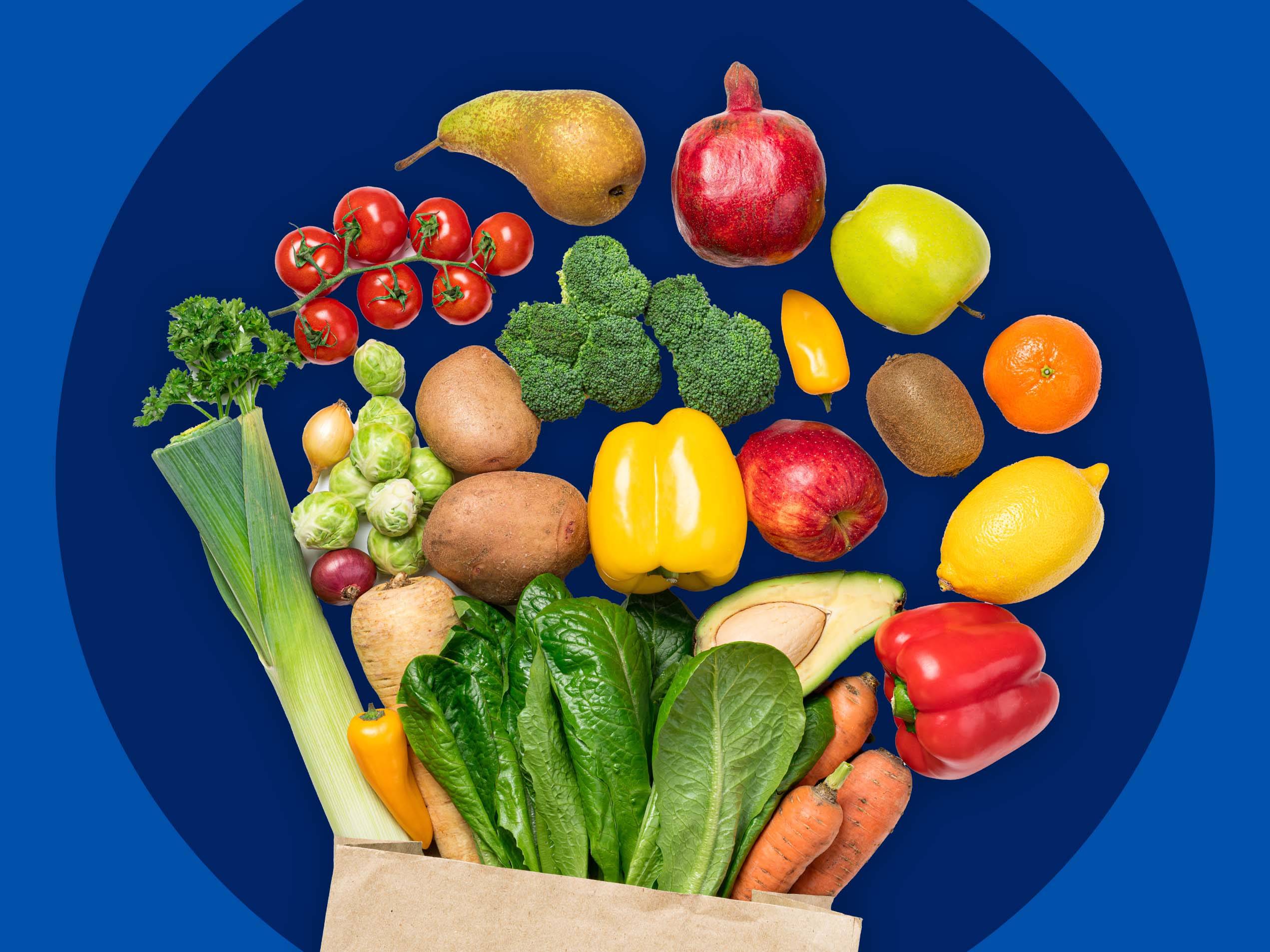 Ein brauner Papierbeutel voller frischem Obst und Gemüse schwebt vor einem blauen Hintergrund.