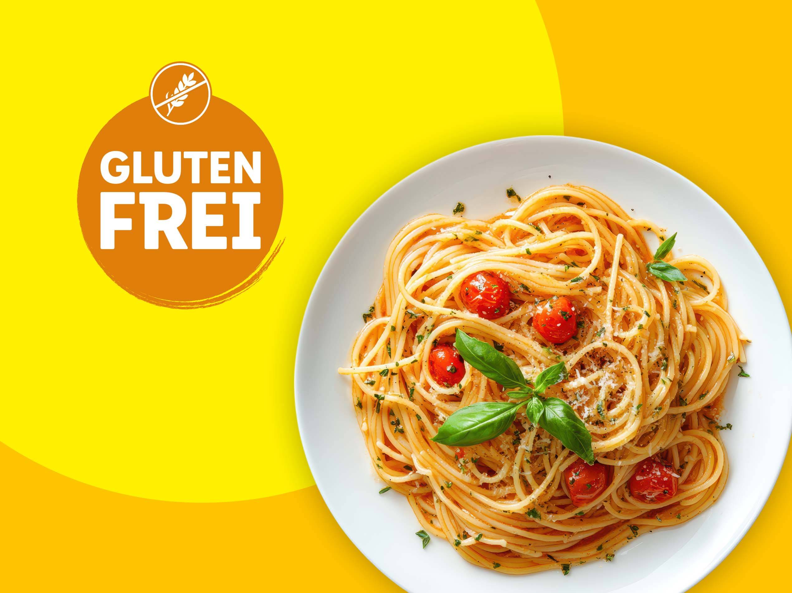 Glutenfreie Spaghetti mit Tomaten und Basilikum auf einem weißen Teller.