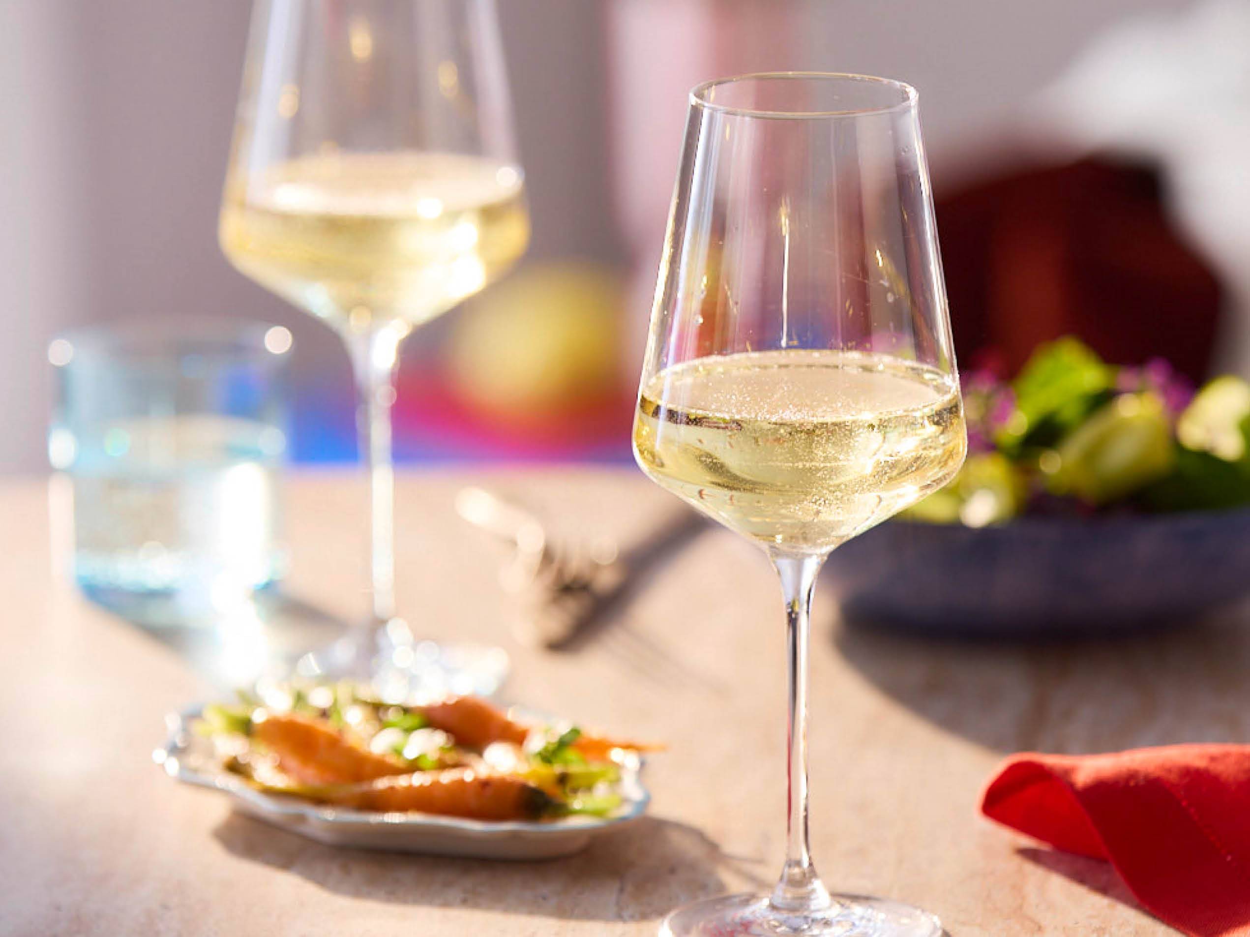 Zwei Gläser Weißwein stehen auf einem Tisch neben einem einem Teller Salat.