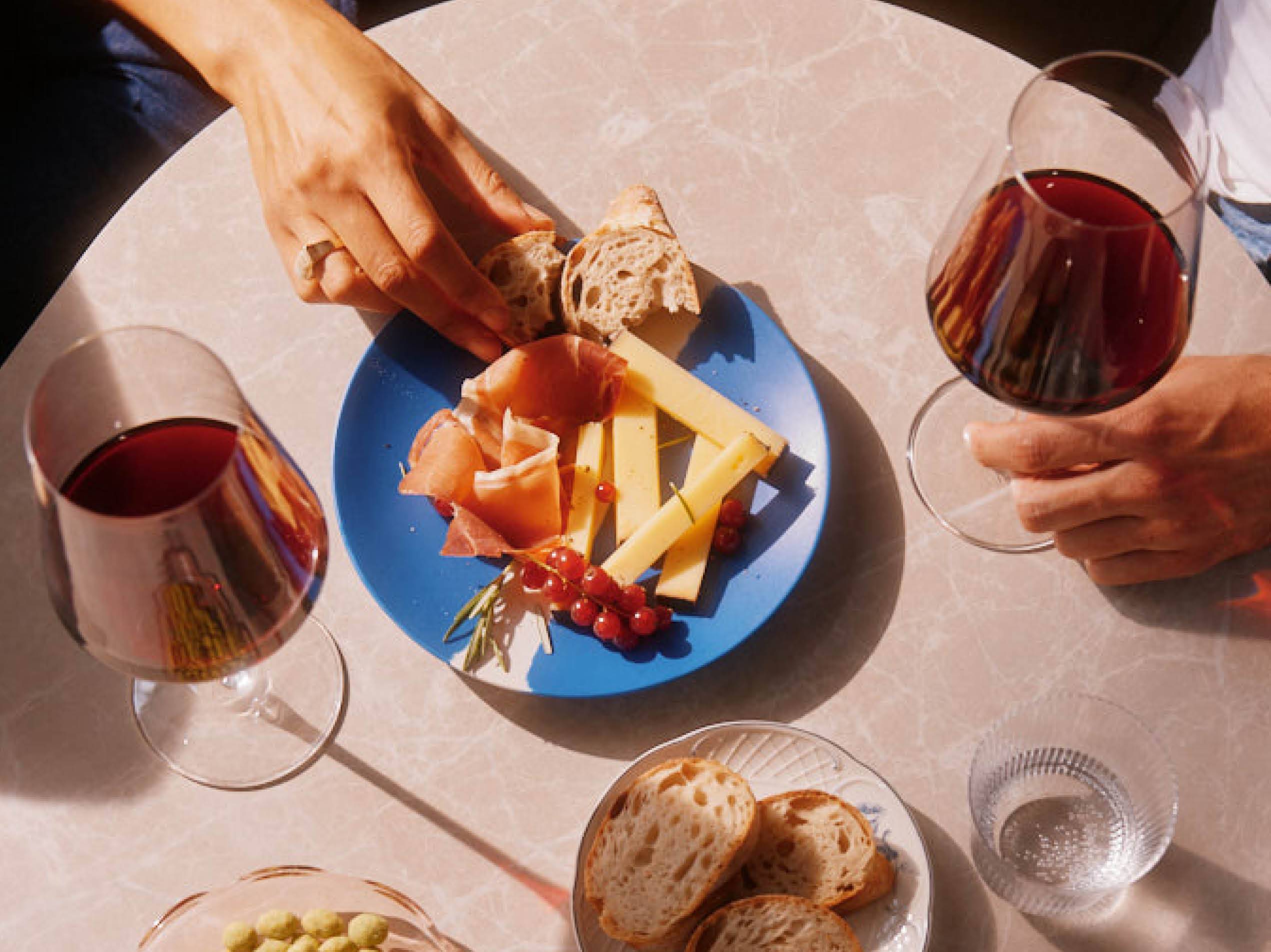 Auf einem Tisch steht eine Auswahl an Käse, Prosciutto sowie Brot und daneben stehen zwei Gläser Wein.