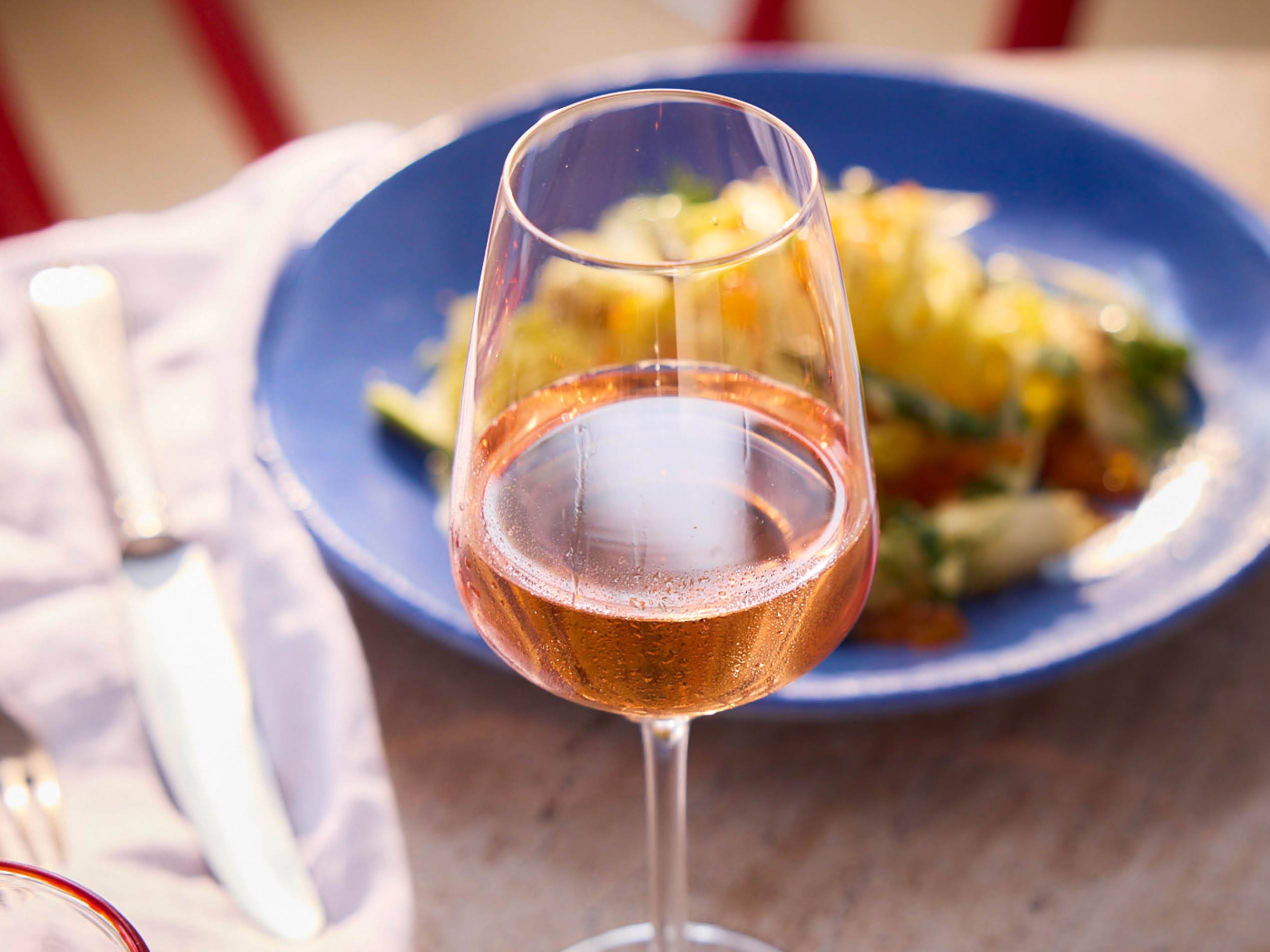 Ein Glas Roséwein steht auf einem Tisch neben einem blauen Teller mit Salat.