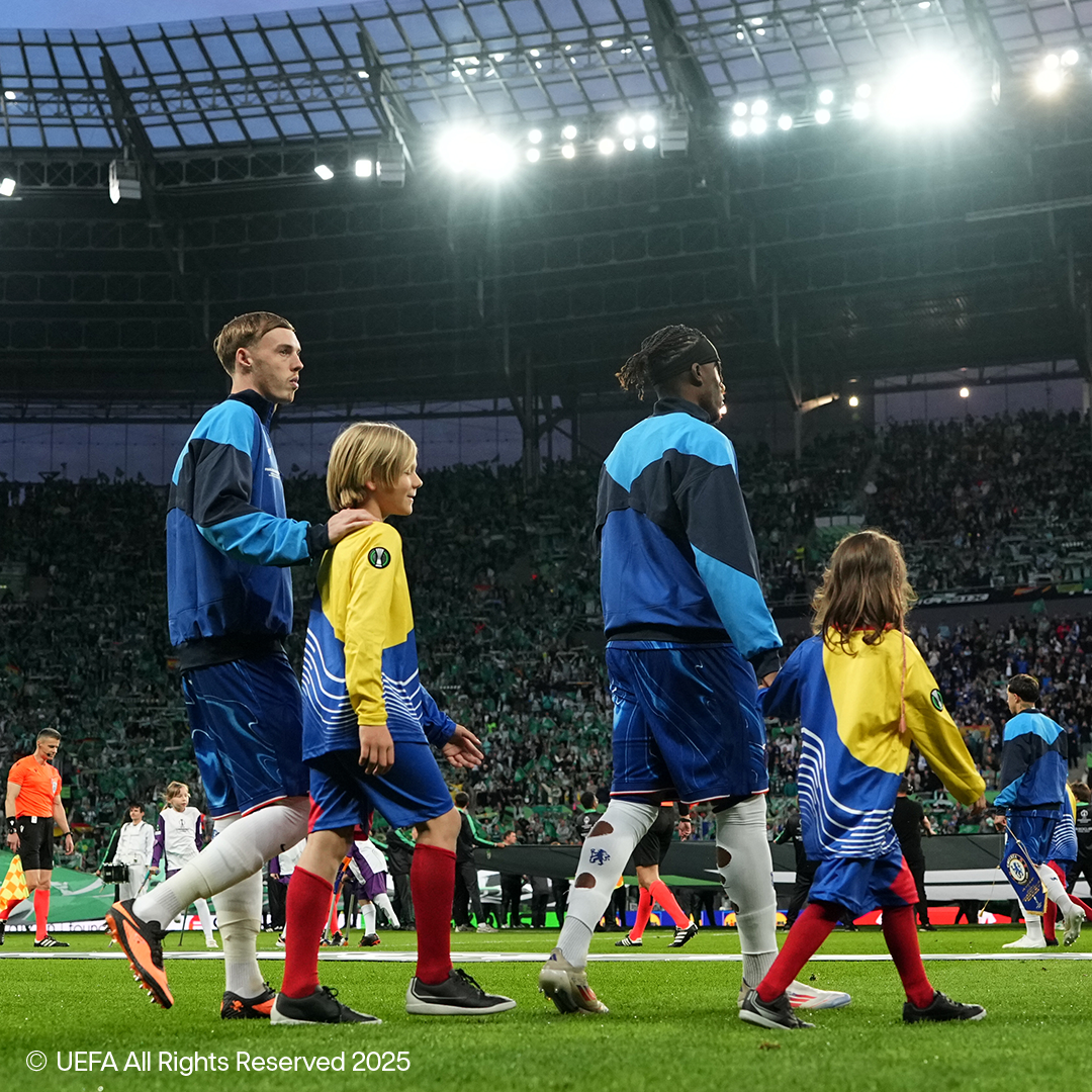 Fußballspieler und Kinder gehen auf dem Feld eines vollen Stadions.
