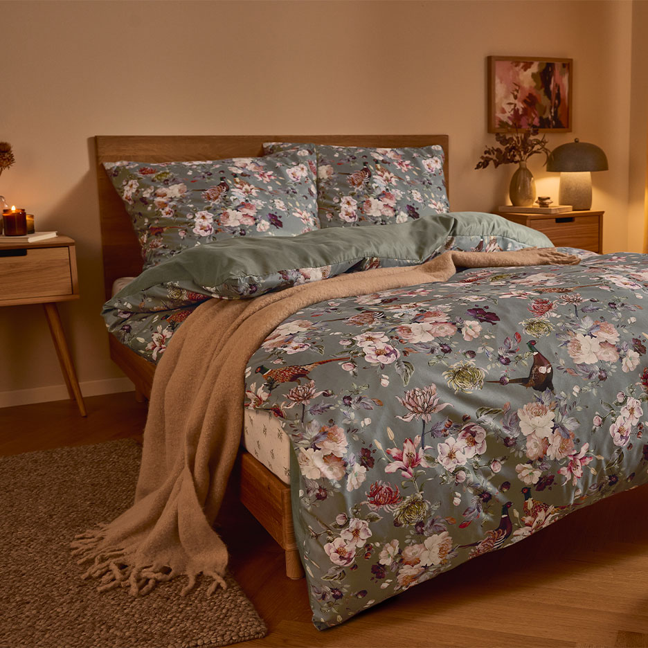 Holzbett mit grüner Blumenbettwäsche und einer braunen Decke.