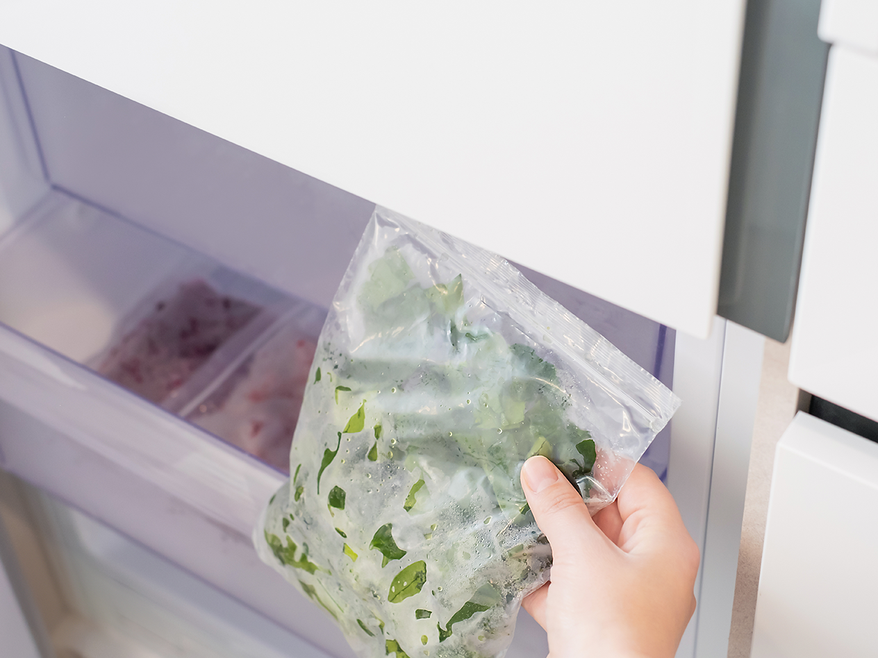 Hand legt Beutel mit gefrorenem Spinat in den Gefrierschrank.