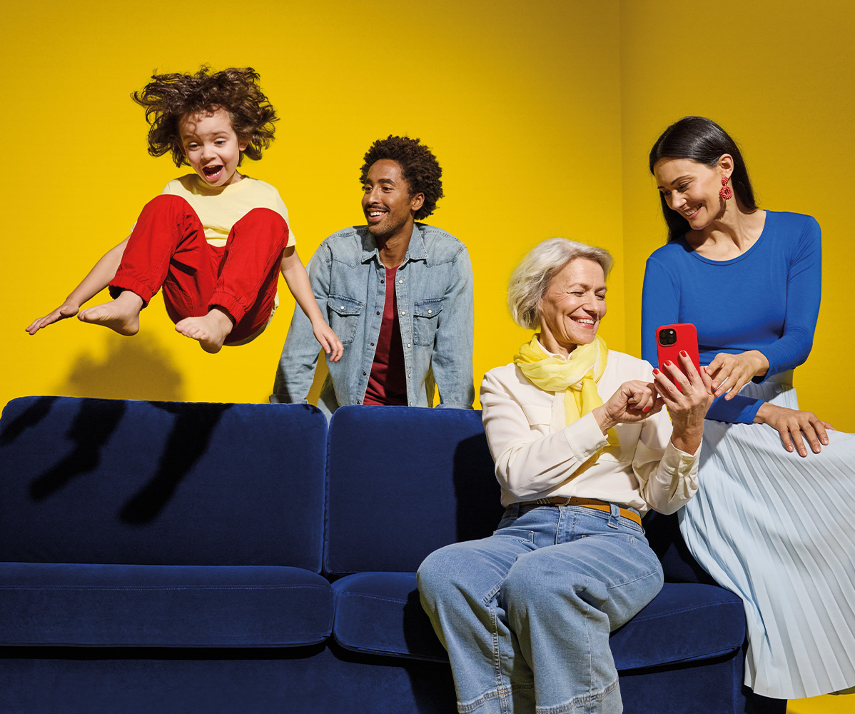 Familie mit Mutter, Vater, Kind und Oma sitzt auf Couch, haben Spaß und sehen sich die Lidl Plus App an