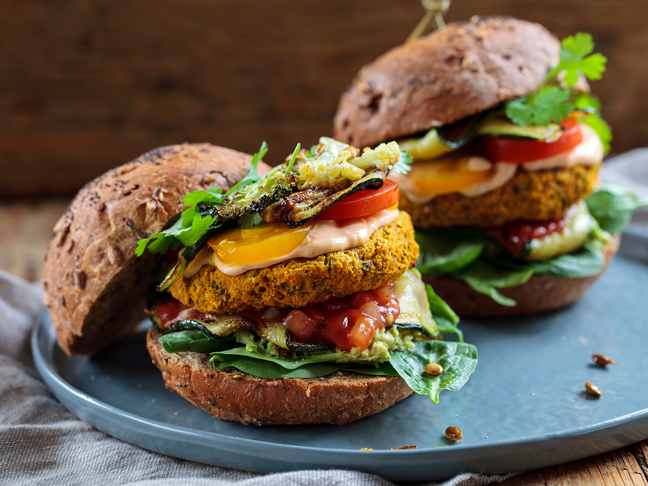 Zwei vegane Burger mit Gemüse, Soße und Vollkornbrötchen auf einem Teller.