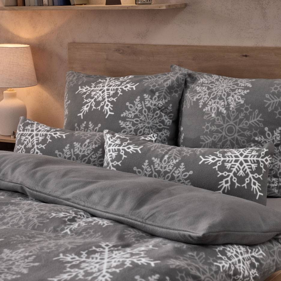 Graue Bettwäsche mit weißen Schneeflocken, mit Kissen und flauschiger Decke.