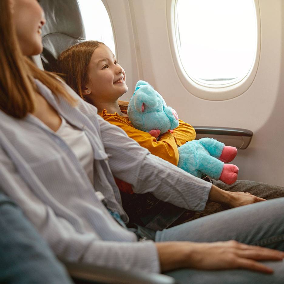 Ein Kind mit einem Plüschtier schaut aus einem Flugzeugfenster neben einem Erwachsenen.