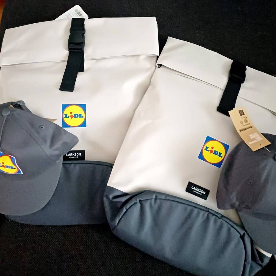 Zwei weiße Rucksäcke mit grauen Details und zwei graue Kappen mit gelbem Logo.