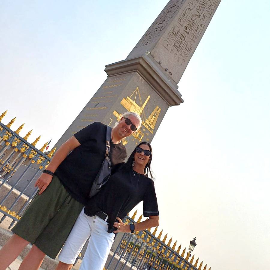 Ein Paar in Sonnenbrillen posiert vor einem Obelisken mit Hieroglyphen.