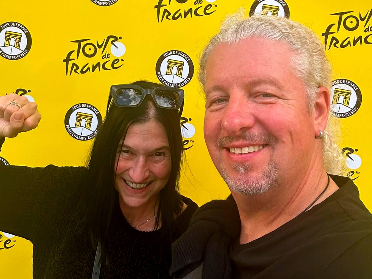 Ein Mann und eine Frau lächeln vor einem gelben Hintergrund mit dem Logo der Tour de France.