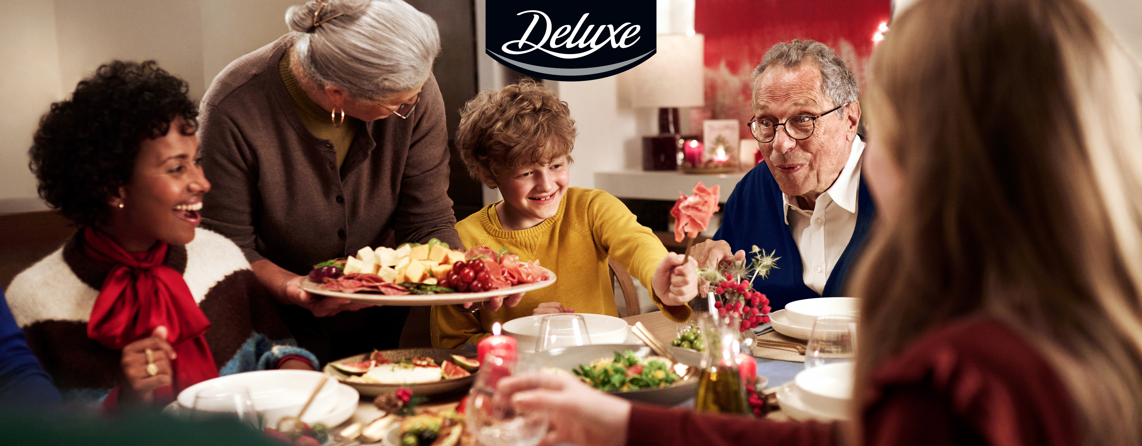 Familie am Esstisch mit Deluxe-Käse- und Wurstplatte.