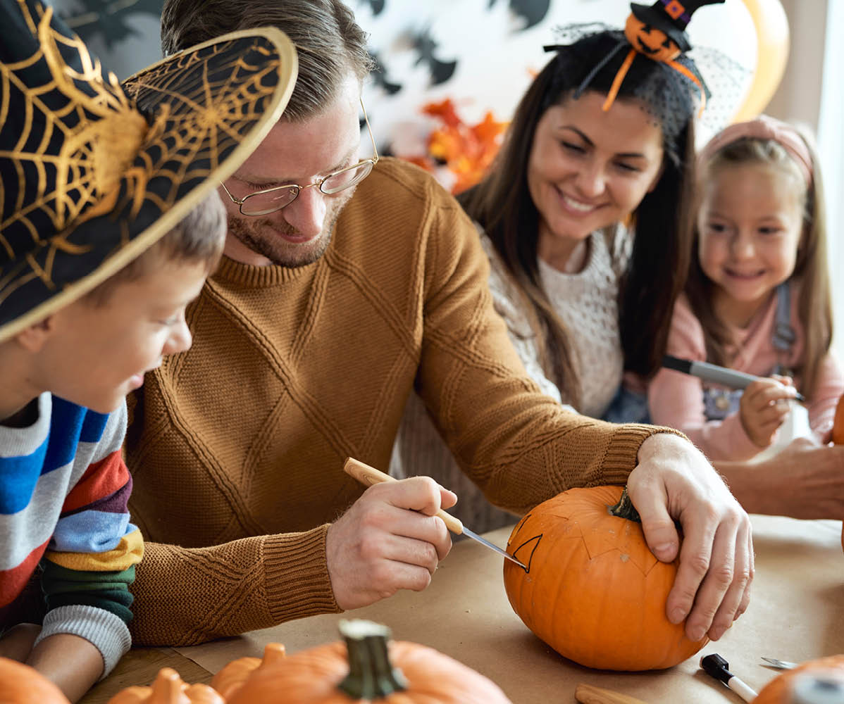 Eine Familie schnitzt Kürbisse für Halloween, der Vater hilft dem Sohn beim Schnitzen.