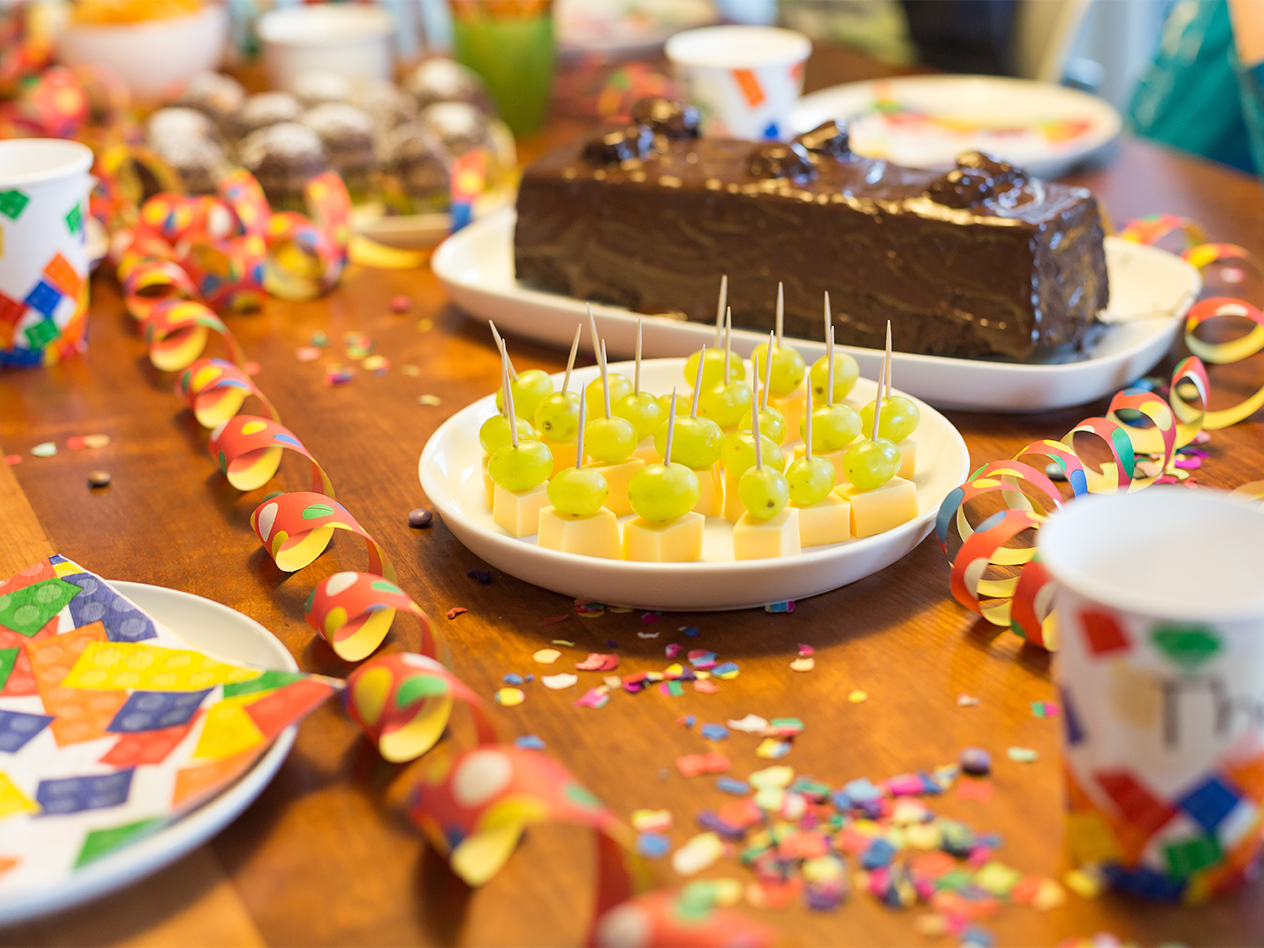 Geburtstagstisch mit Schokoladenkuchen, Käse-Trauben-Spießen und bunten Dekorationen.