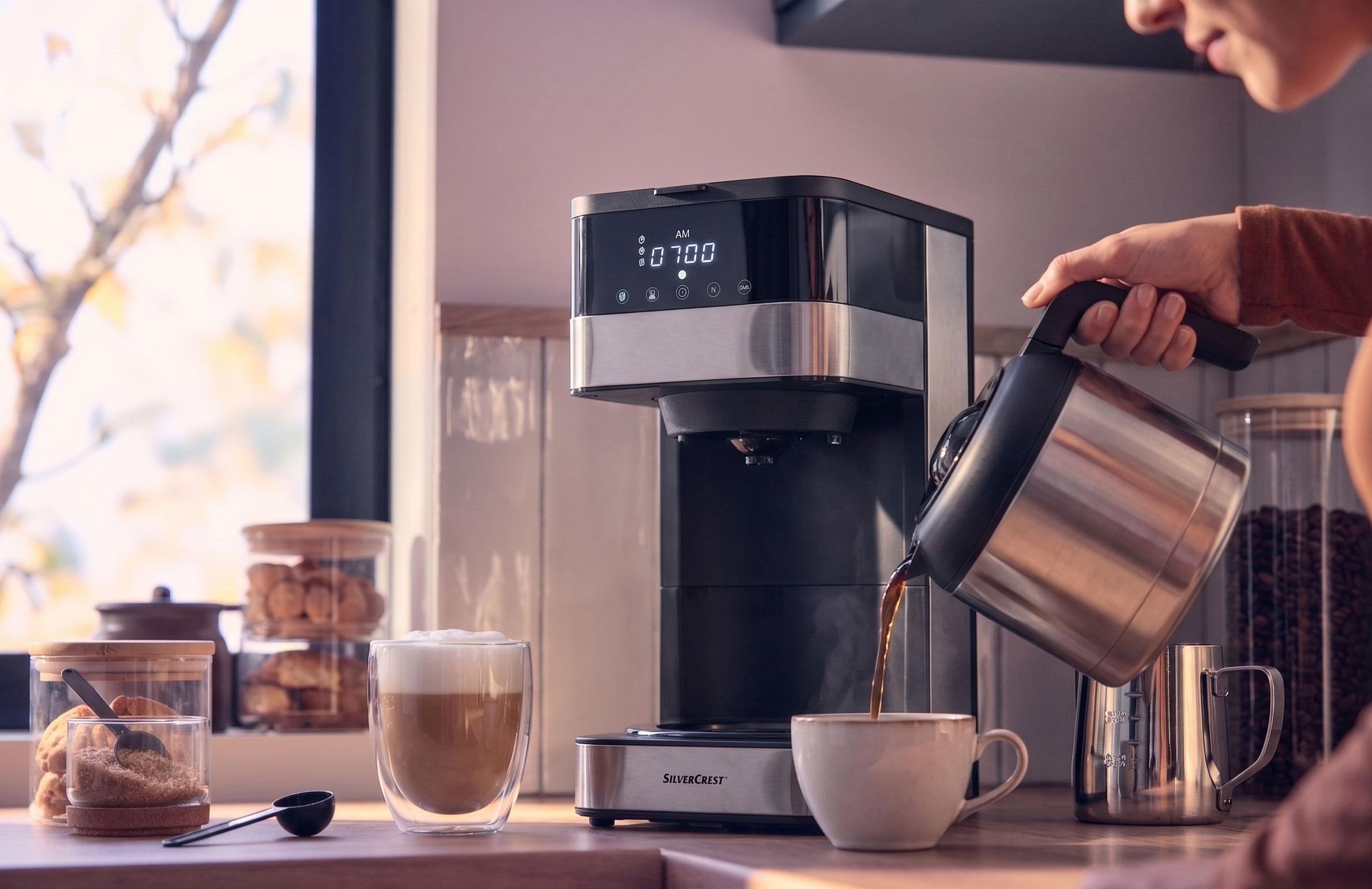Kaffeemaschine gießt Kaffee in eine Tasse, mit einem Latte und Keksen auf der Theke.