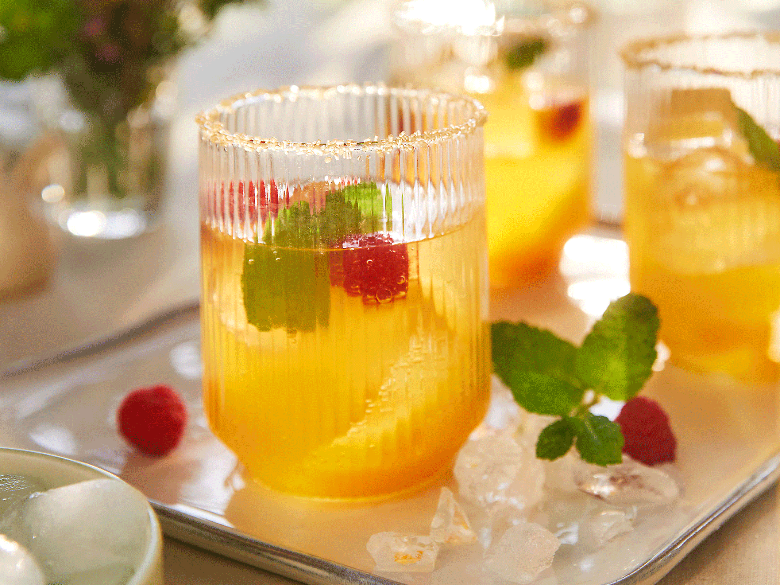 Erfrischende Sommergetränke mit Himbeeren, Minze und Eiswürfeln auf einem Tablett.