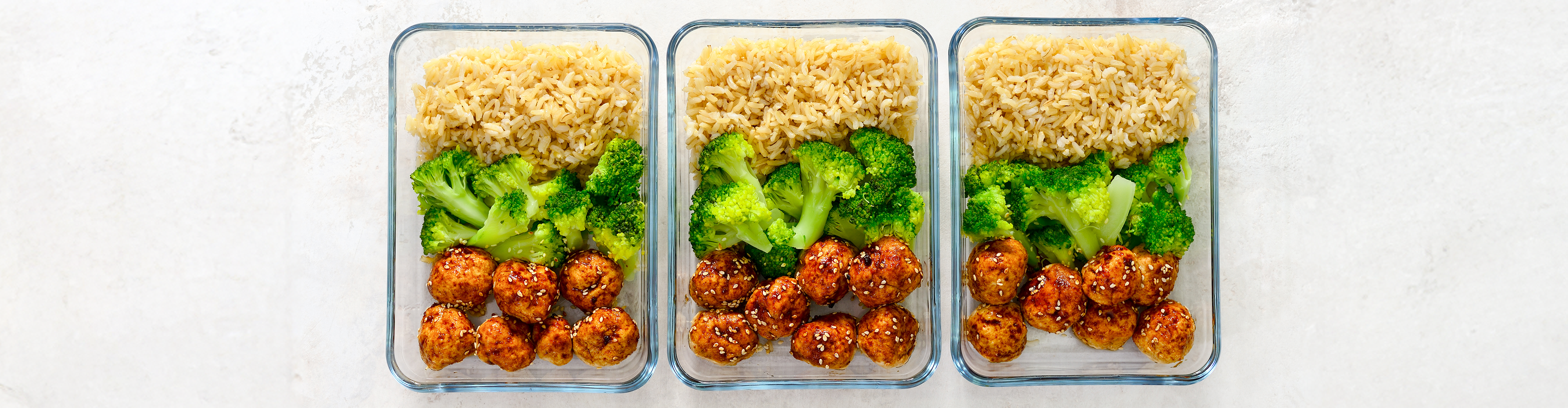 Drei Mahlzeiten in Glasbehältern mit Reis, Brokkoli und Hähnchenbällchen.