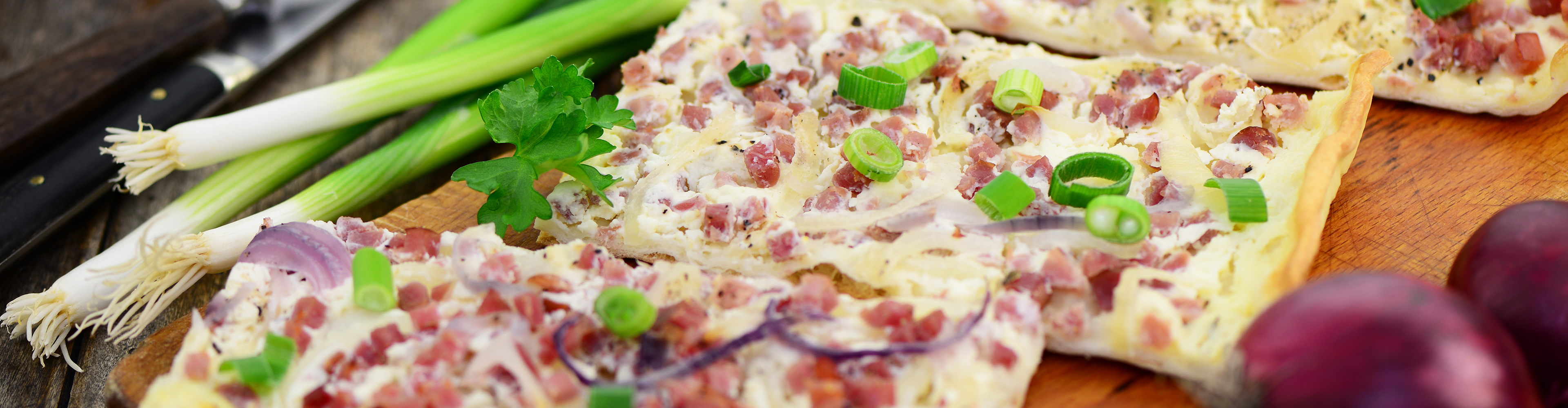 Flammkuchen mit Speck, Zwiebeln und Frühlingszwiebeln auf einem Holzbrett