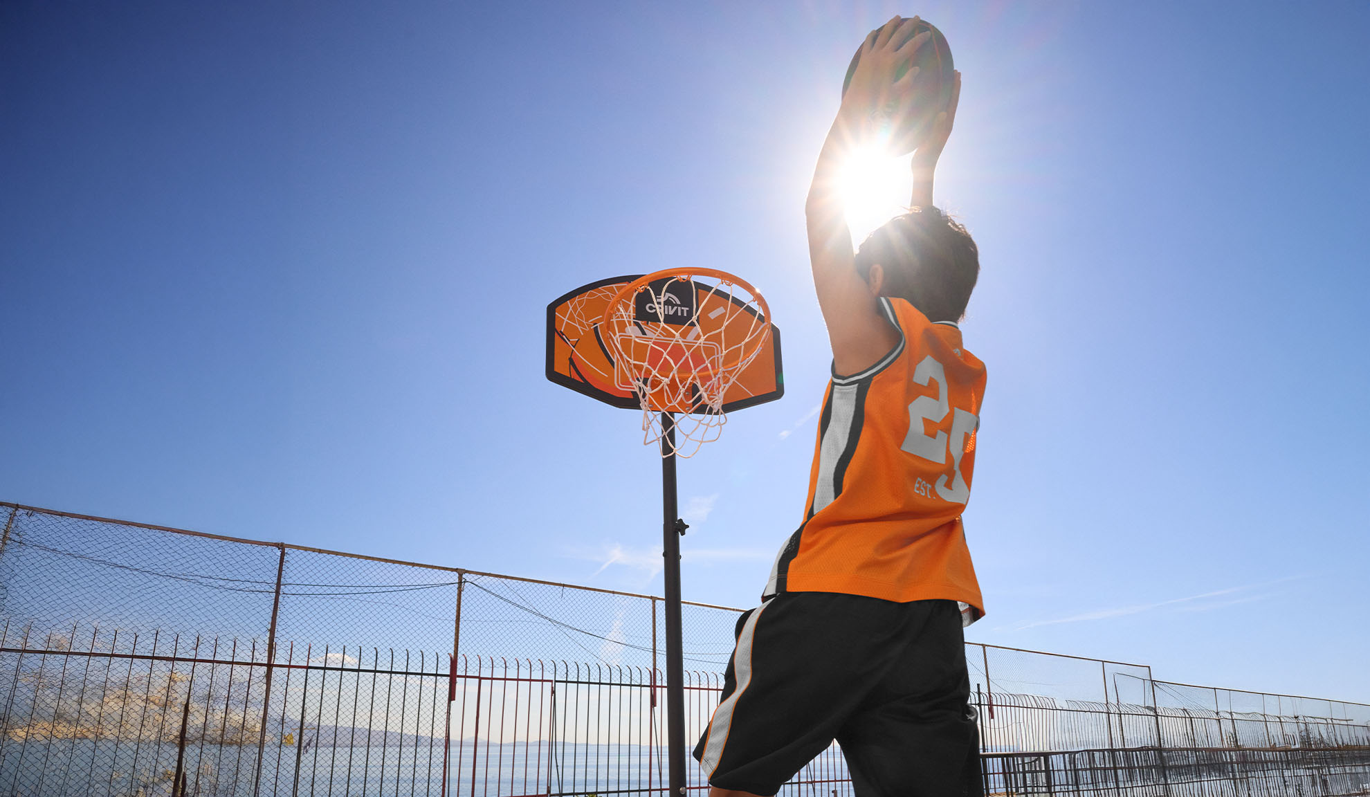 Junge im Basketballtrikot wirft Körbe im Freien unter strahlender Sonne.