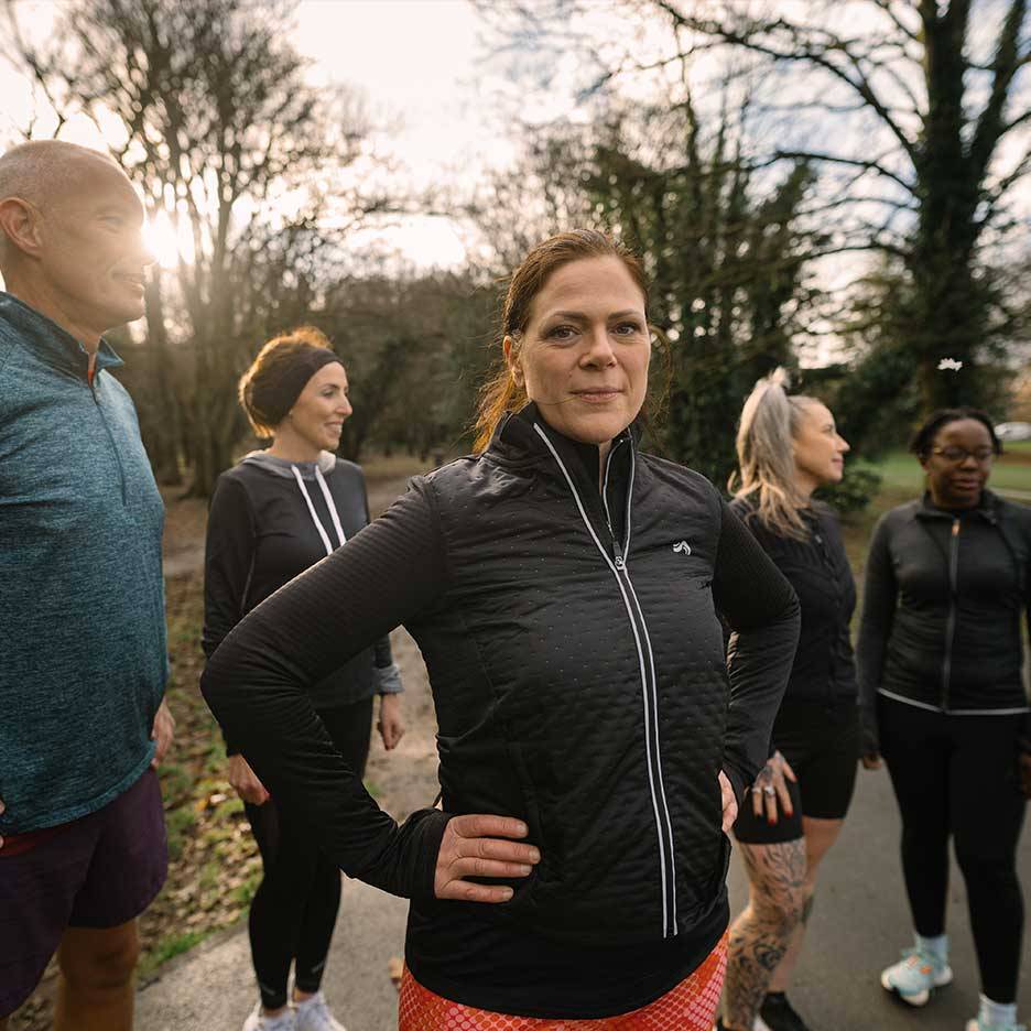 Gruppe von Personen in Sportkleidung, darunter eine Frau in einer schwarzen Steppjacke, im Freien.