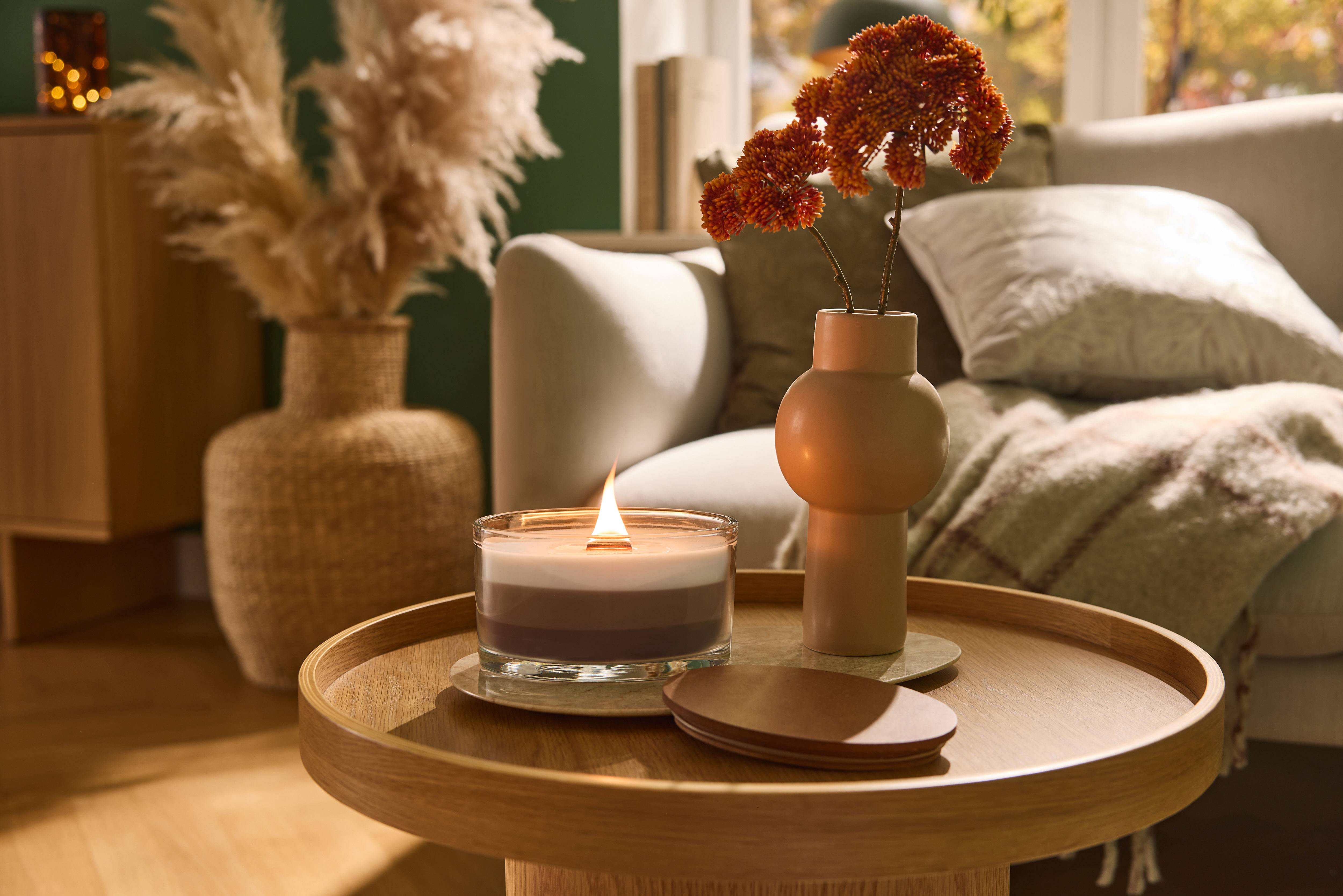 Brennende Kerze und Vase mit Blumen auf einem Holztisch im Wohnzimmer.