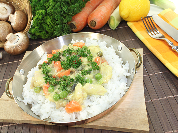 Hähnchenfrikassee mit Reis in einer Kupferschale, umgeben von frischem Gemüse.