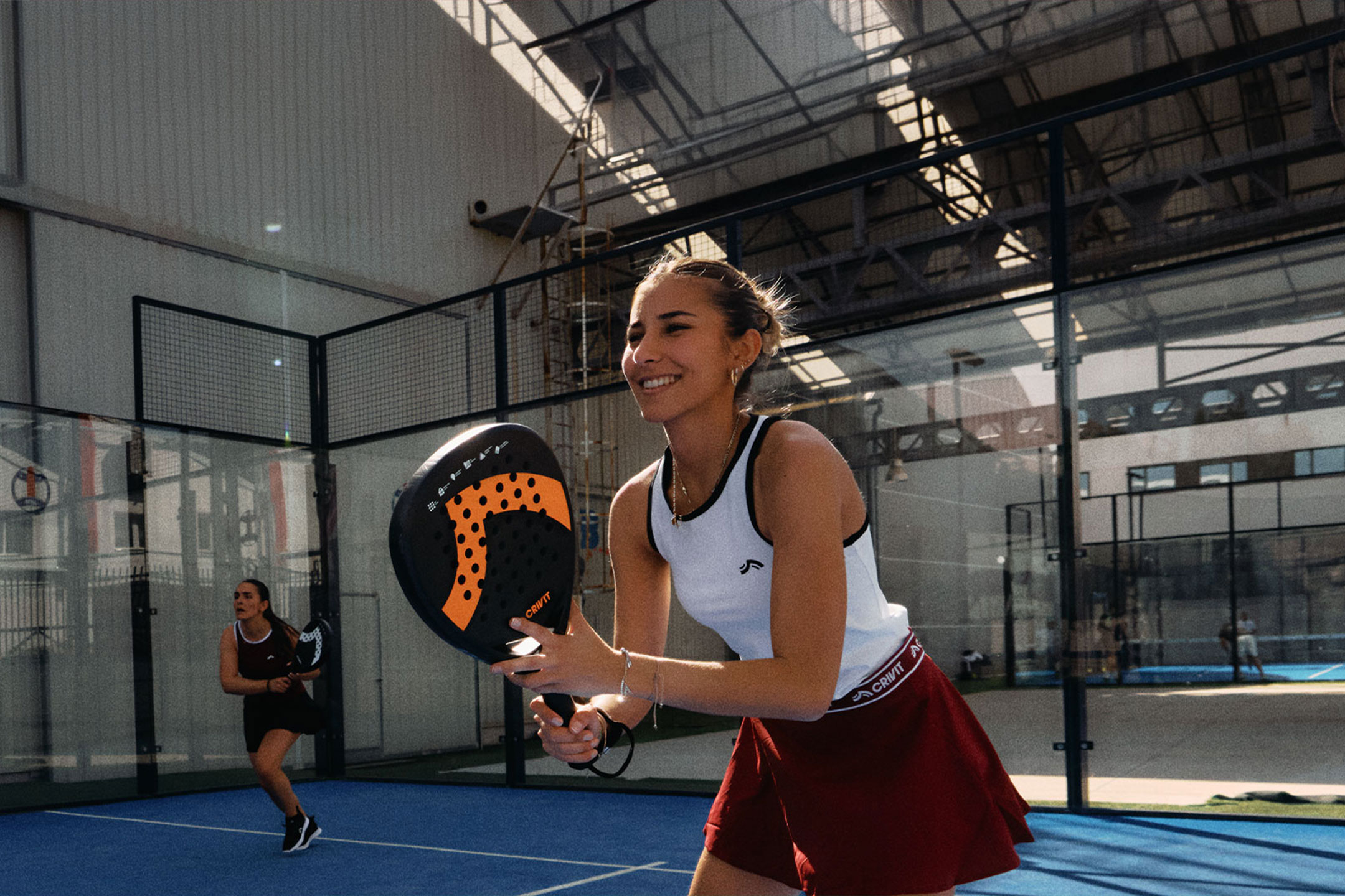 KI-generiert: Zwei Frauen spielen Padel-Tennis, eine lächelt und hält einen Schläger, auf einem blauen Platz.